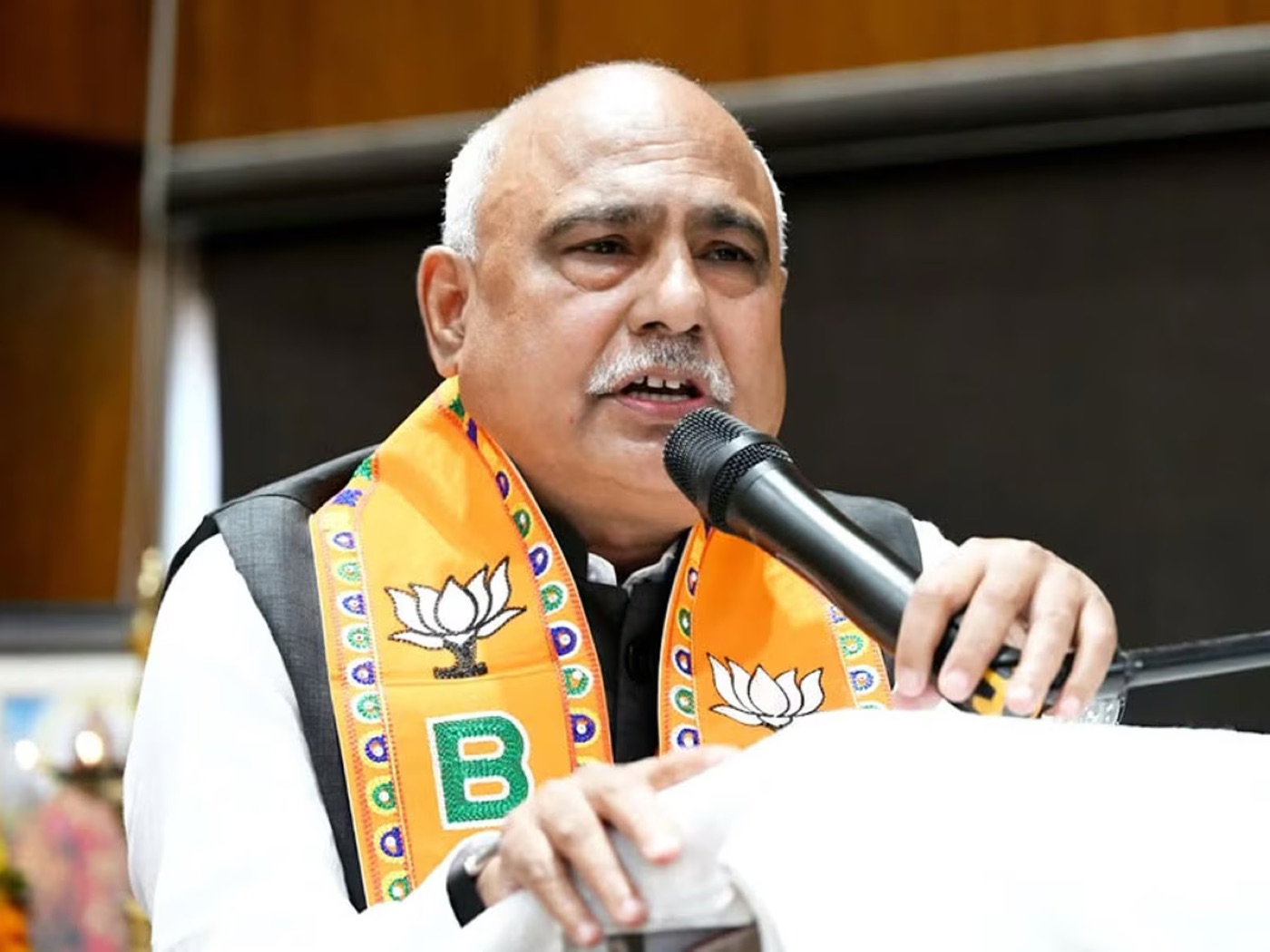 Hemant Khandelwal speaking at a microphone wearing a party stole